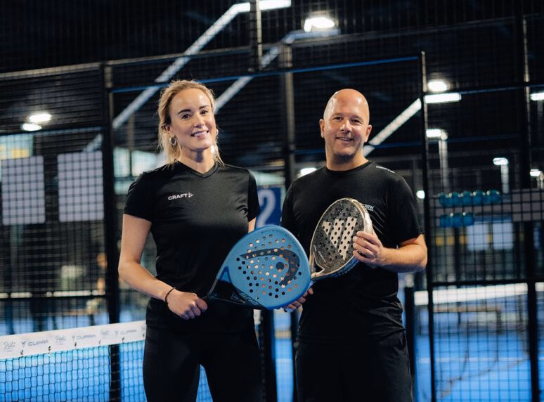 Twee sporters poseren met padelrackets op een indoor padelbaan tijdens een zakelijk sportevent.
