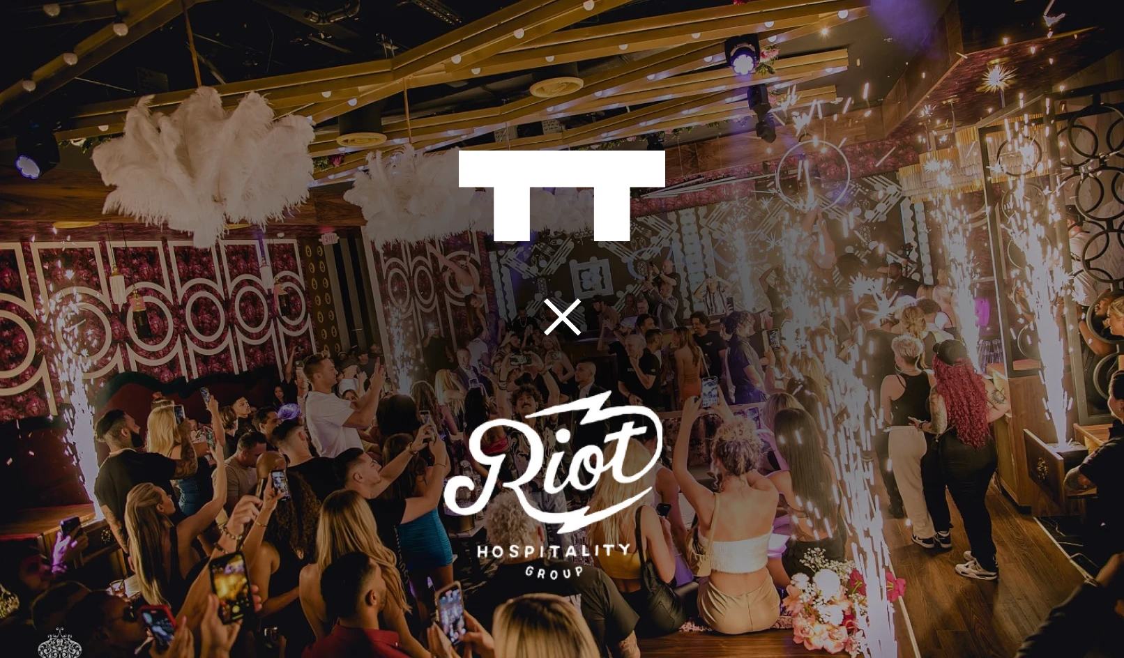 Crowded nightclub scene with people dancing, holding phones, and sparklers lighting the room.