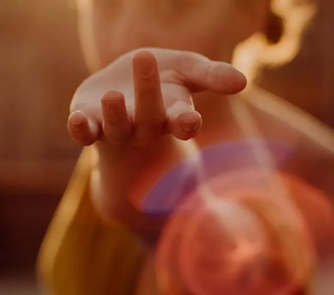 A woman holding up her hand surrounded by light to symbolize the pleasure of pelvic floorgasm.