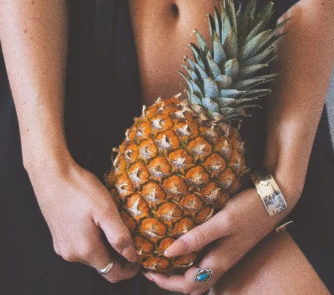 A woman holding a prickly-leaved pineapple in front of her body to symbolize dyspareunia.