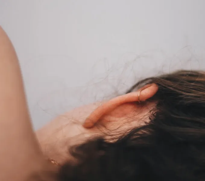 A close-up of a woman's head from the back, she's lying on her side and her hair is pulled back to reveal her ear and neck.