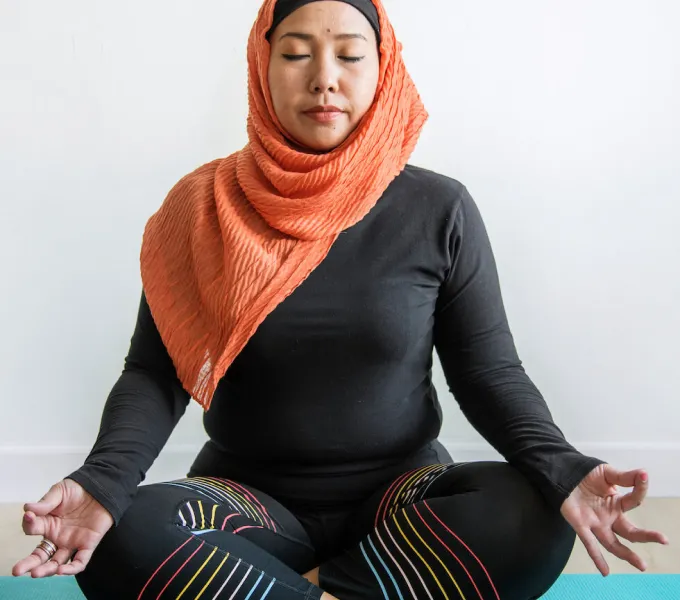 An Islamic woman meditating on a yoga mat.