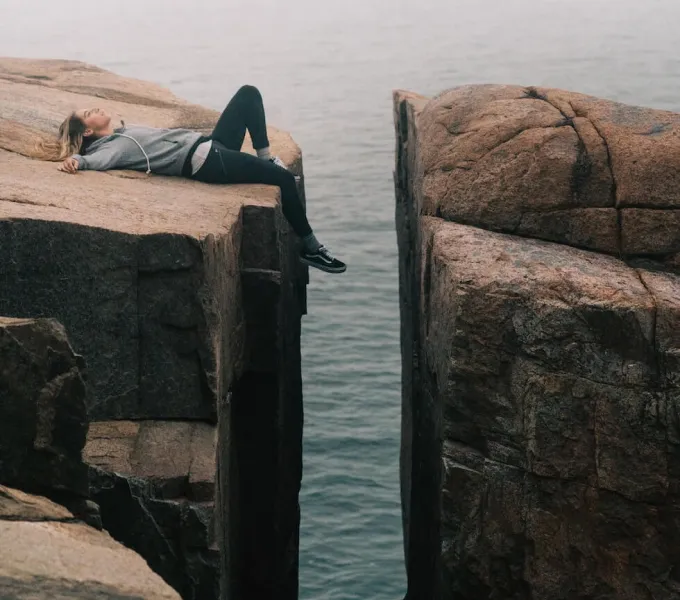 A woman lying next to a huge gap in a rock face.