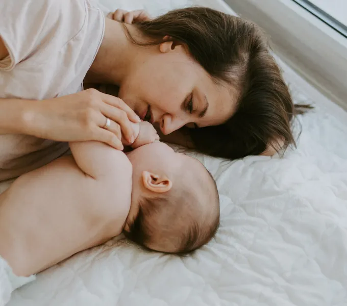 A mother lying face to face with her adorable baby in bed.