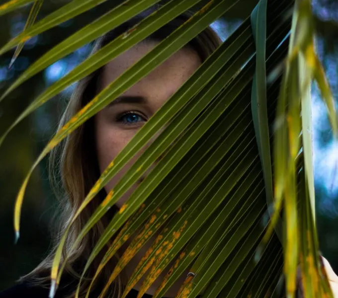 A woman standing behind a large plant so that only her bright blue eye is visble.