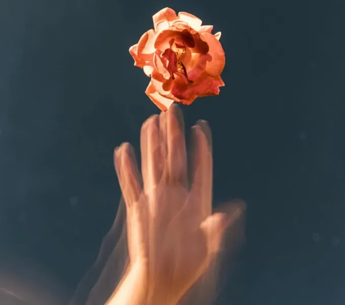 A photo of a woman's hand that looks like its vibrating as it touches a flower.