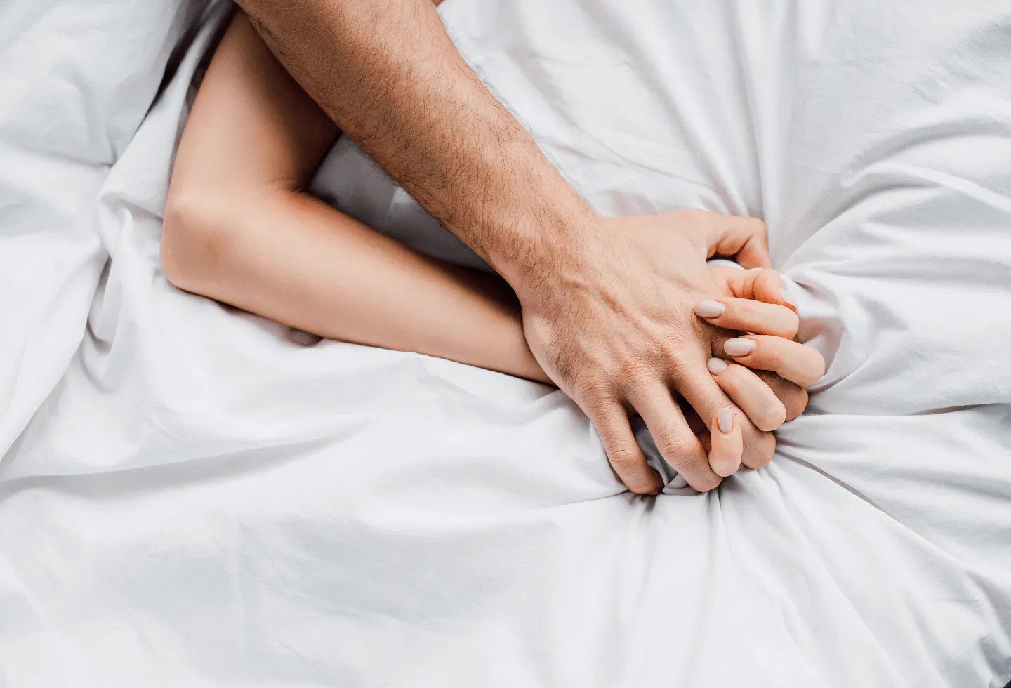 Two people holding hands in bed representing intimacy after cancer treatment.