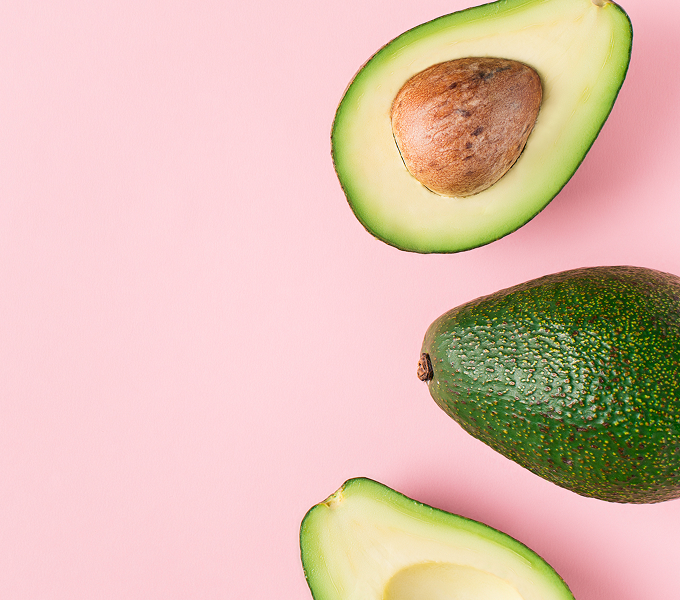 Avocados on a pink backdrop representing Diet to Gain Muscle Mass for women