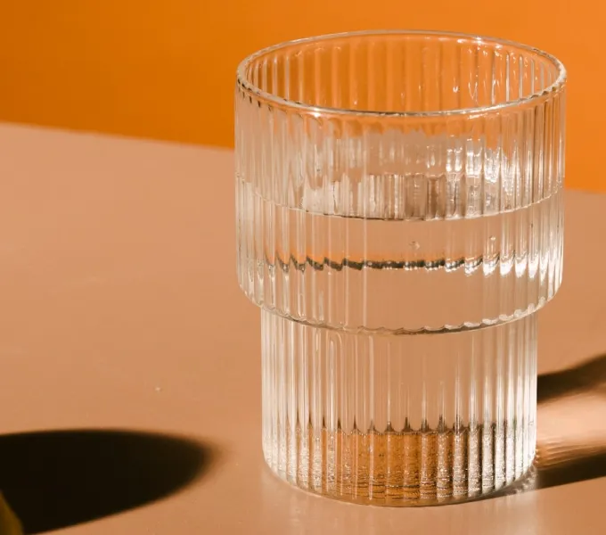 Glass of water on a table with orange background. Represents hydration strategies to avoid back and pelvic pain.