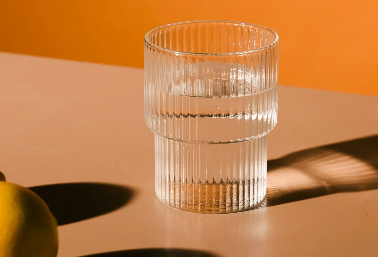 Glass of water on a table with orange background. Represents hydration strategies to avoid back and pelvic pain.