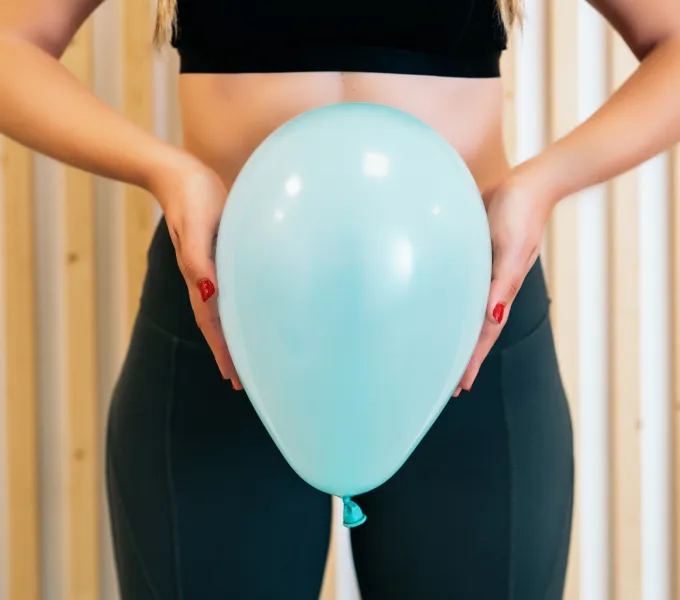 Woman holding inflated balloon in front of her pelvis, representing pelvic floor function what's normal and not normal.