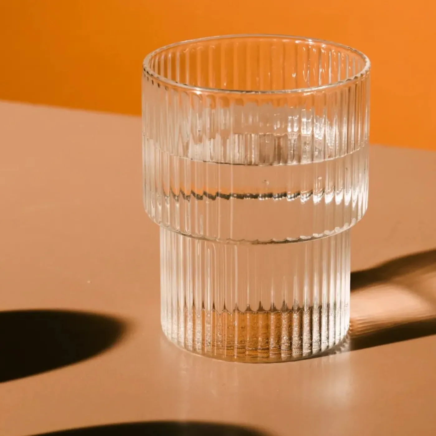 Glass of water on a table with orange background. Represents hydration strategies to avoid back and pelvic pain.