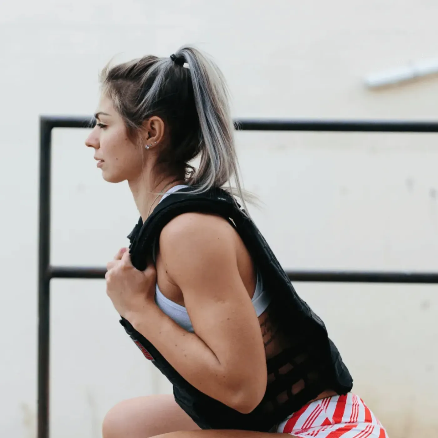 Side profile of a woman doing a squat wearing a weighted vest.