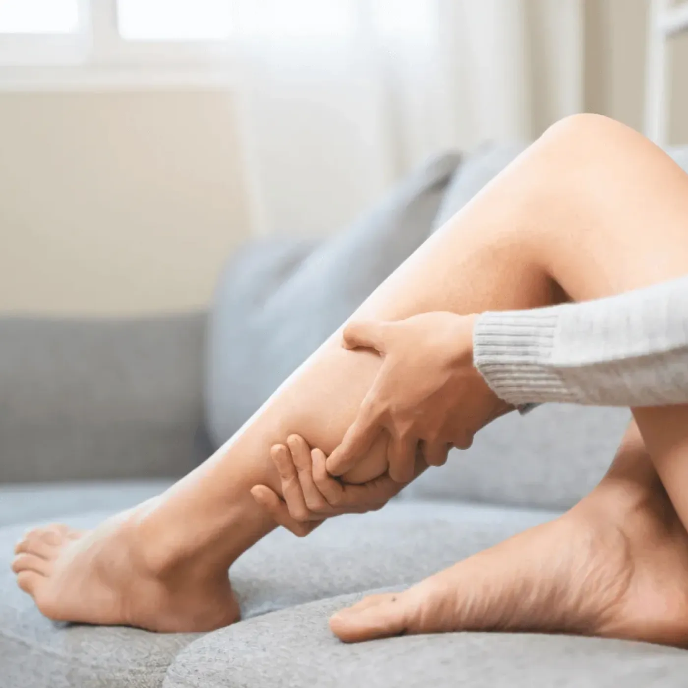 Woman sitting on the couch and holding her leg symbolizing bone pain or muscle pain.