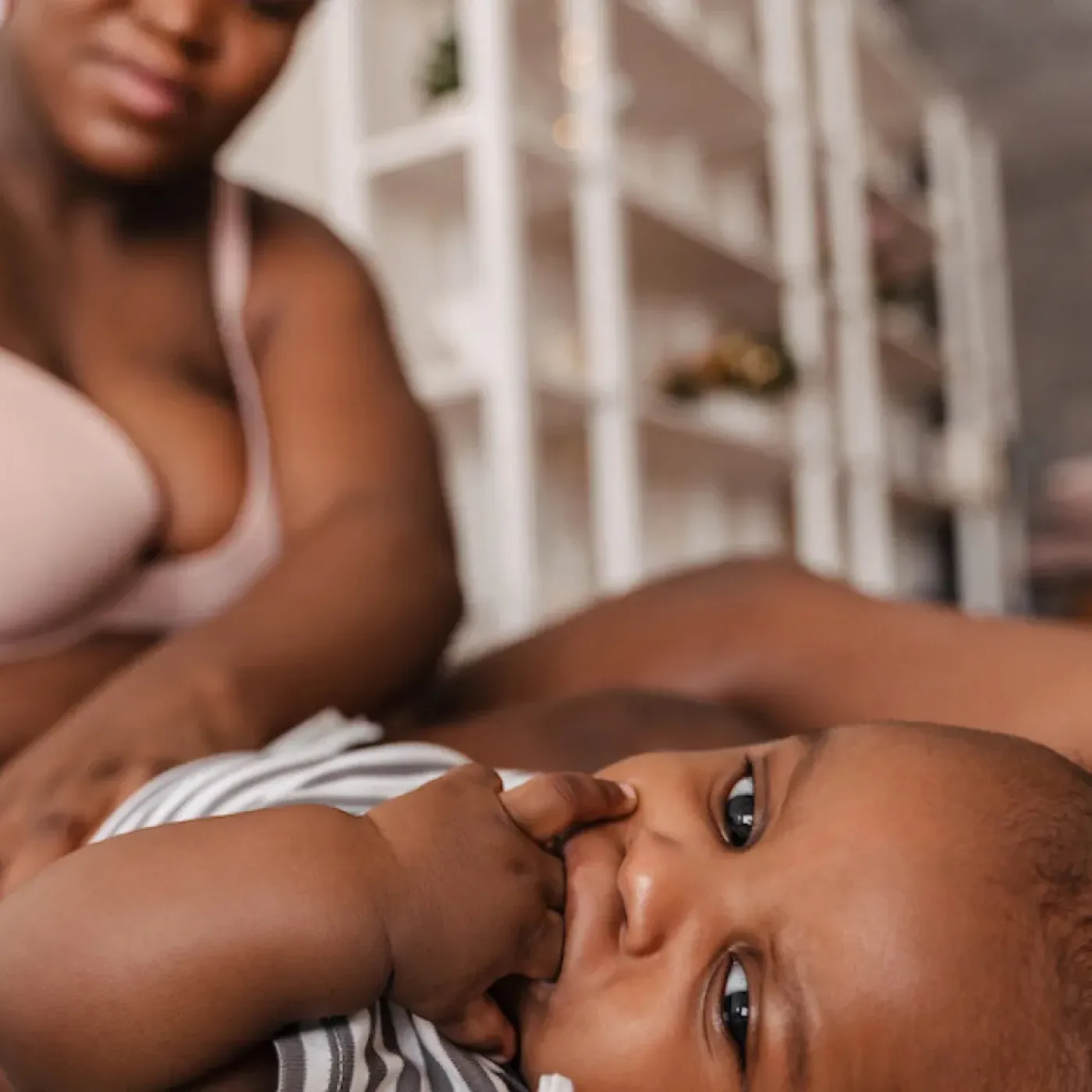 A postpartum mom sitting on her bed, changing her baby's diaper.