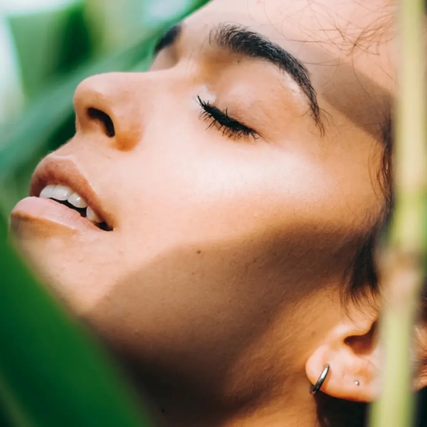 A woman surrounded by lush greenery looking relaxed and self-aware.