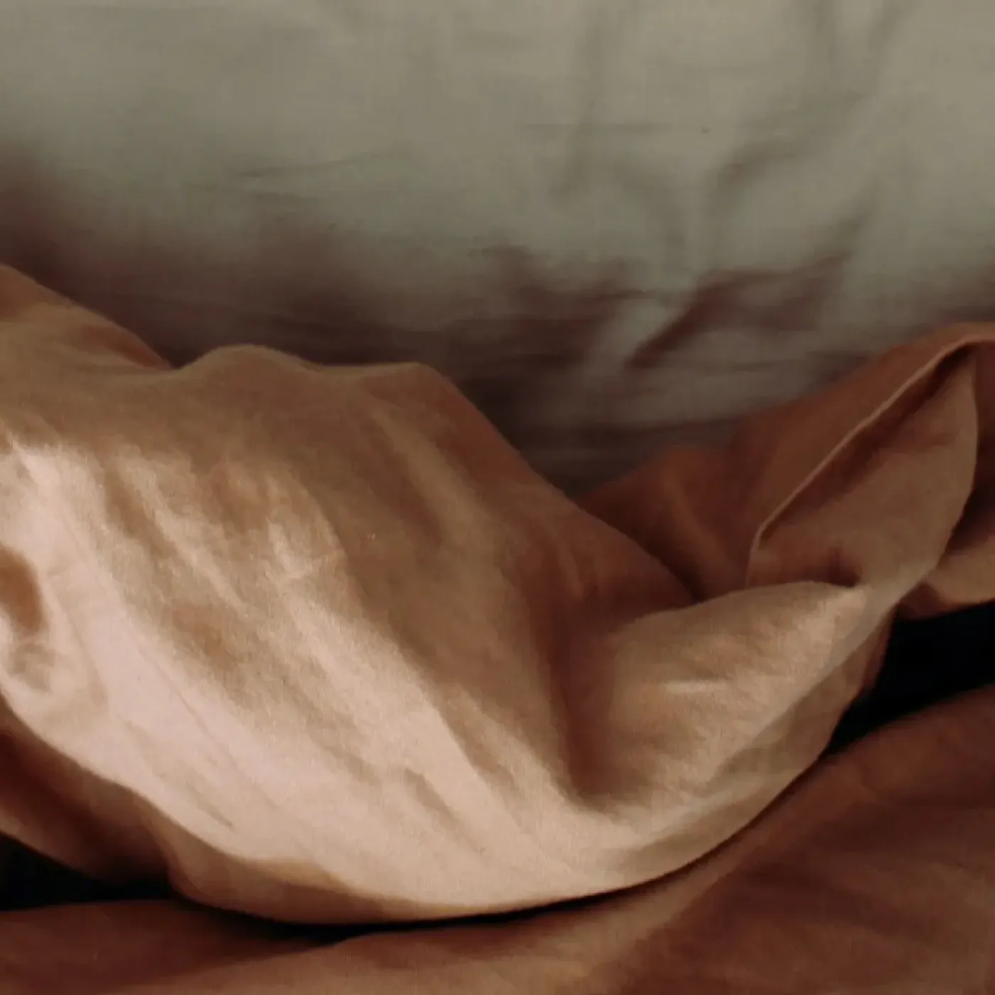 A beige-colored bedspread crumpled up on a bed.