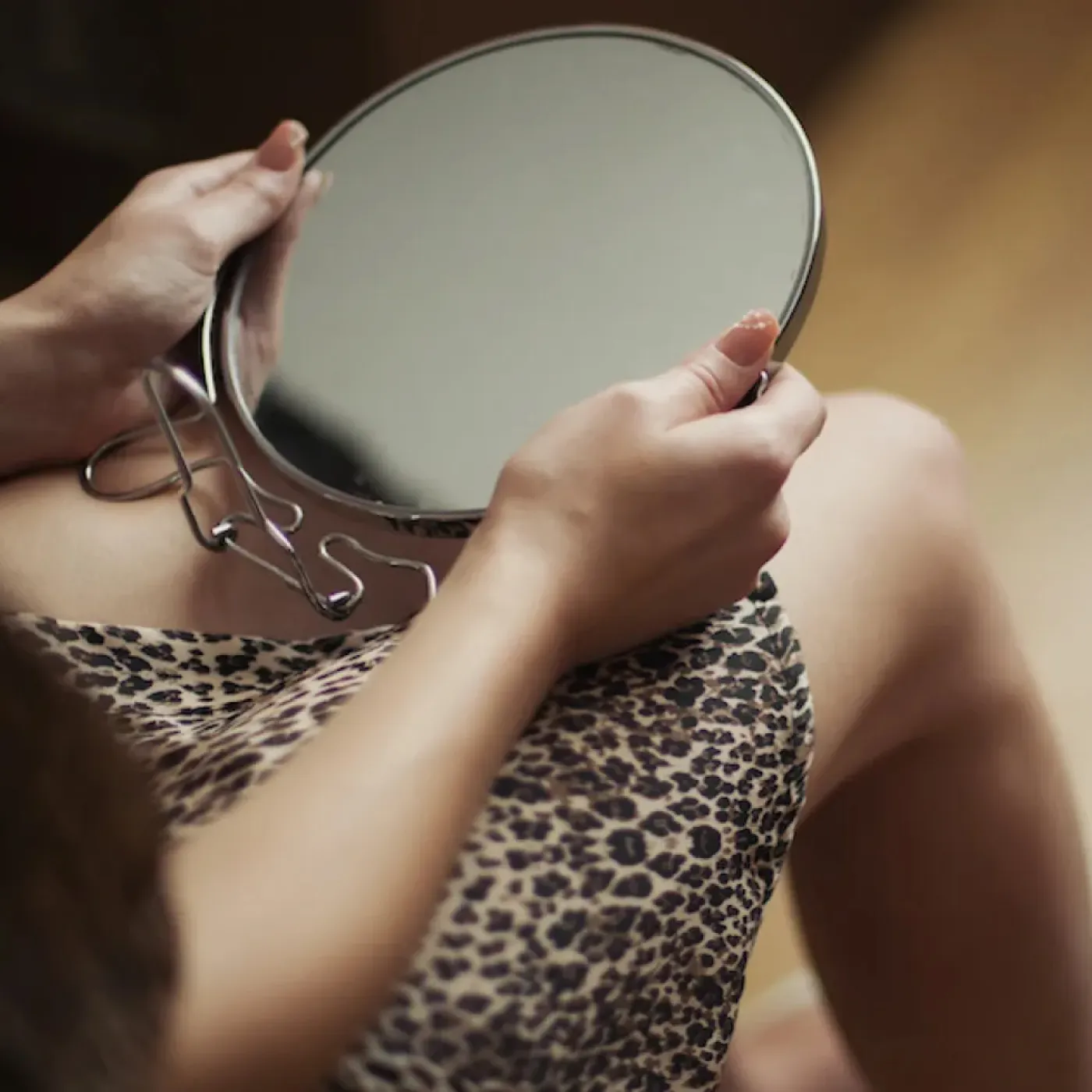 A woman holding a mirror that she's about to use to get a closer look at her clitoris.
