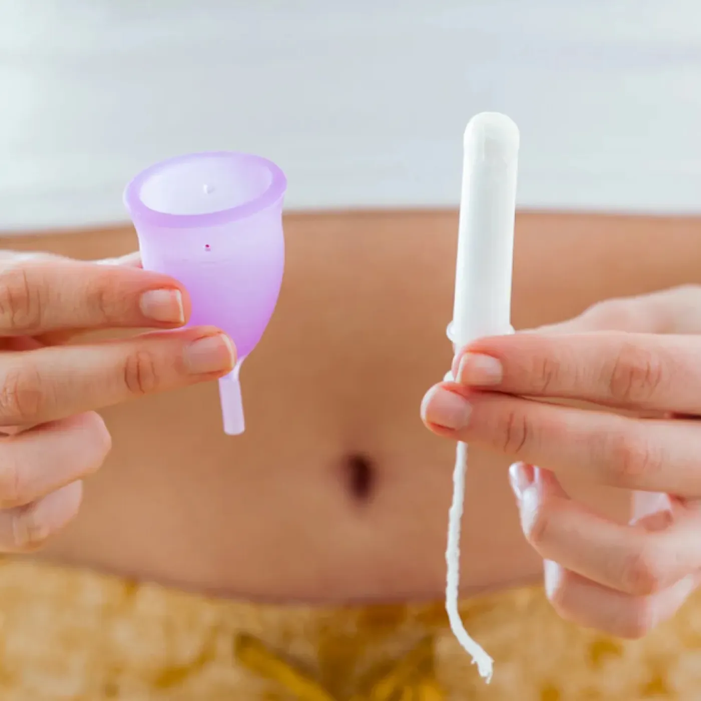A woman holding up a menstrual cup in one hand and a tampon in the other.