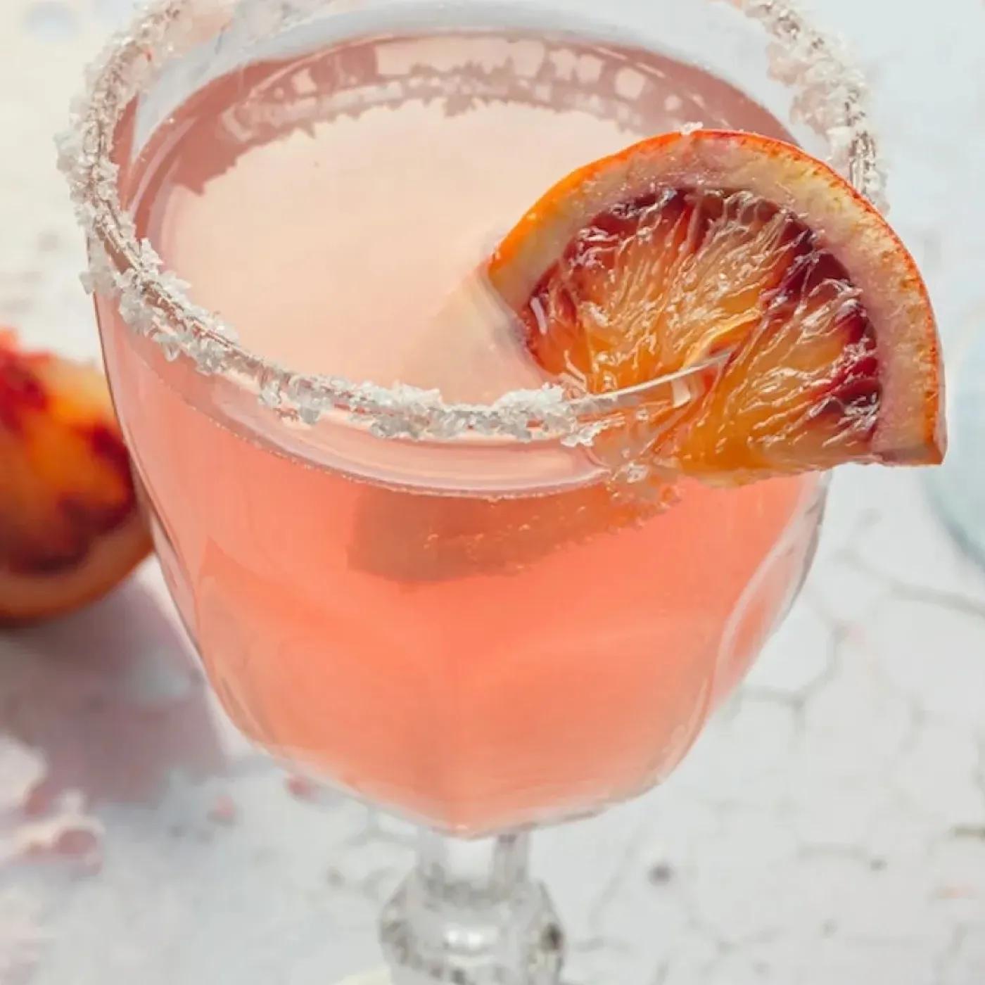 A pink cocktail in crystal stemware with a blood orange garnish and salt rim for a story about bladder irritants.