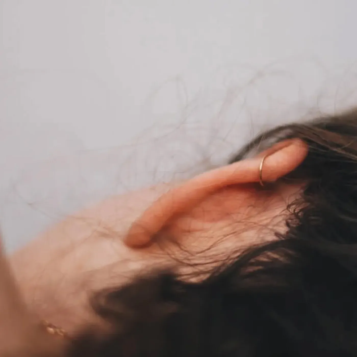 A close-up of a woman's head from the back, she's lying on her side and her hair is pulled back to reveal her ear and neck.
