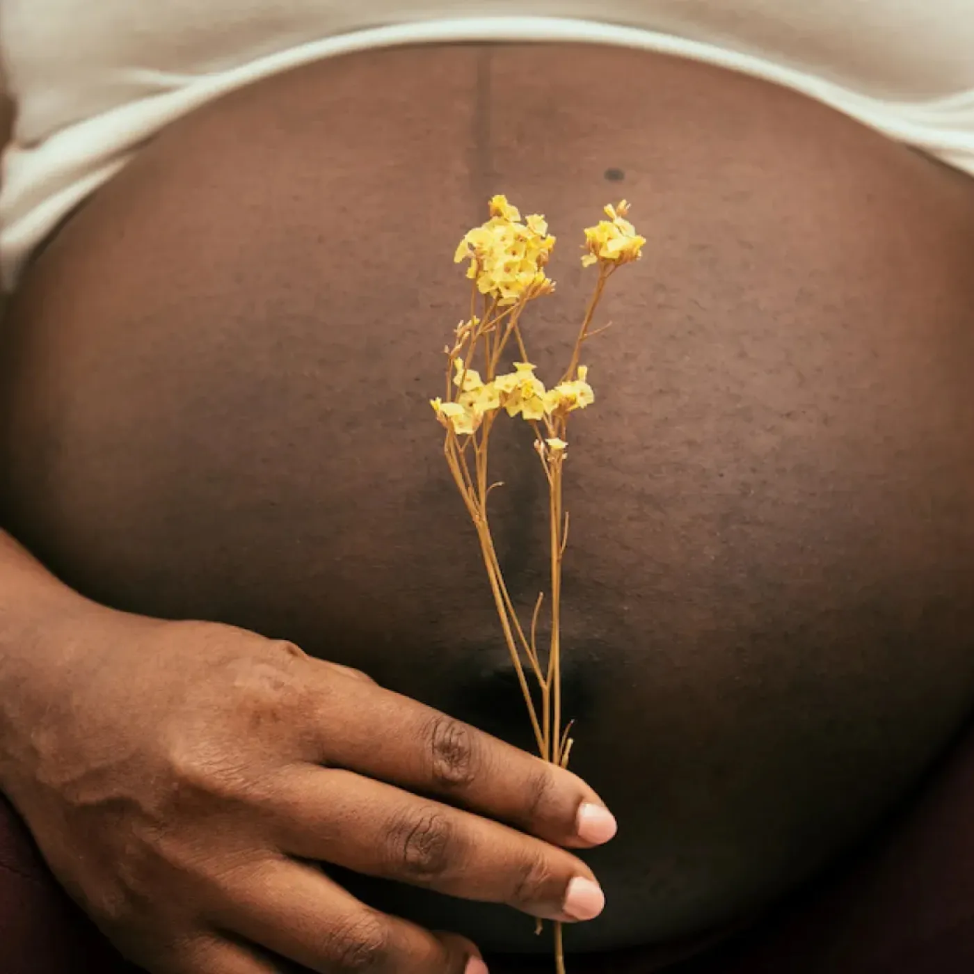 A black pregnant woman holding a small yellow flower in front of her belly.