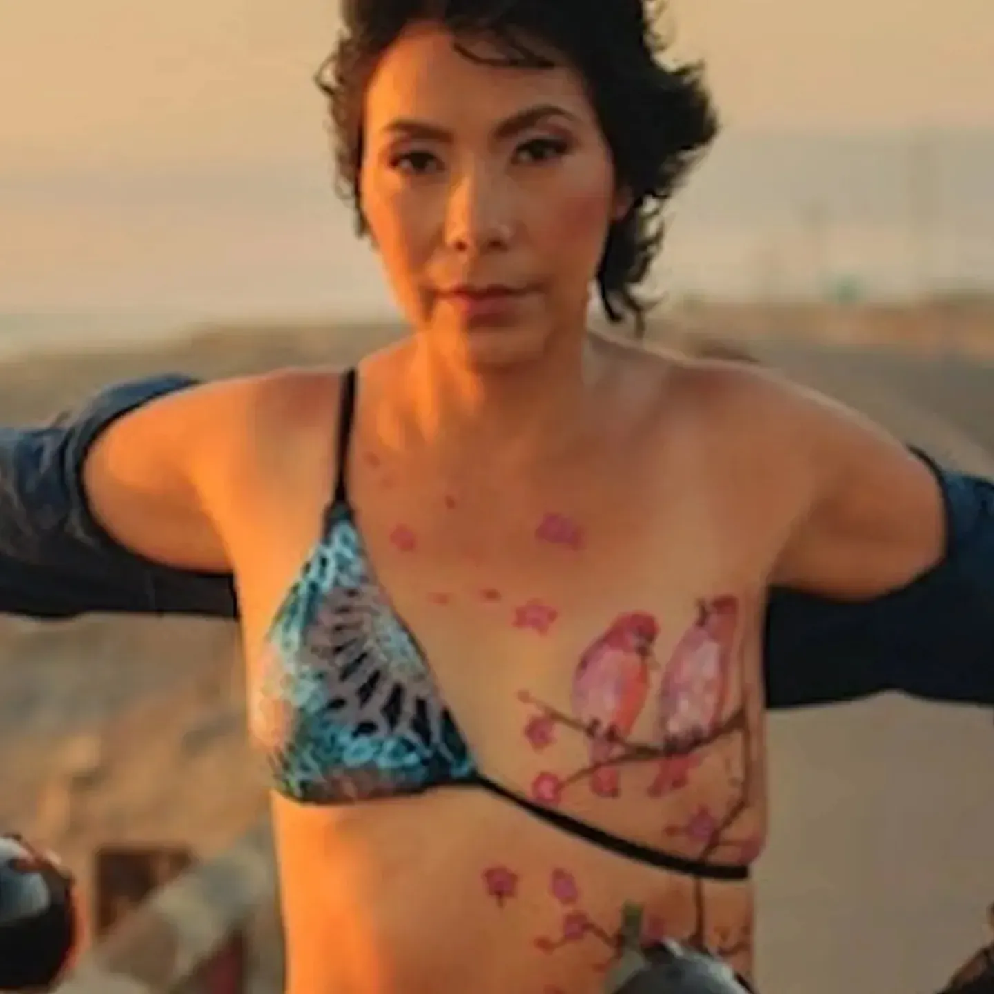 A breast cancer survior sitting confidently astride a motorcycle with a tattoo of birds over her surgery scar.