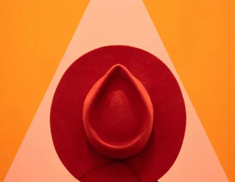 A photo of a woman wearing a red hat in front of a big triangle to symbolize vaginal pain.