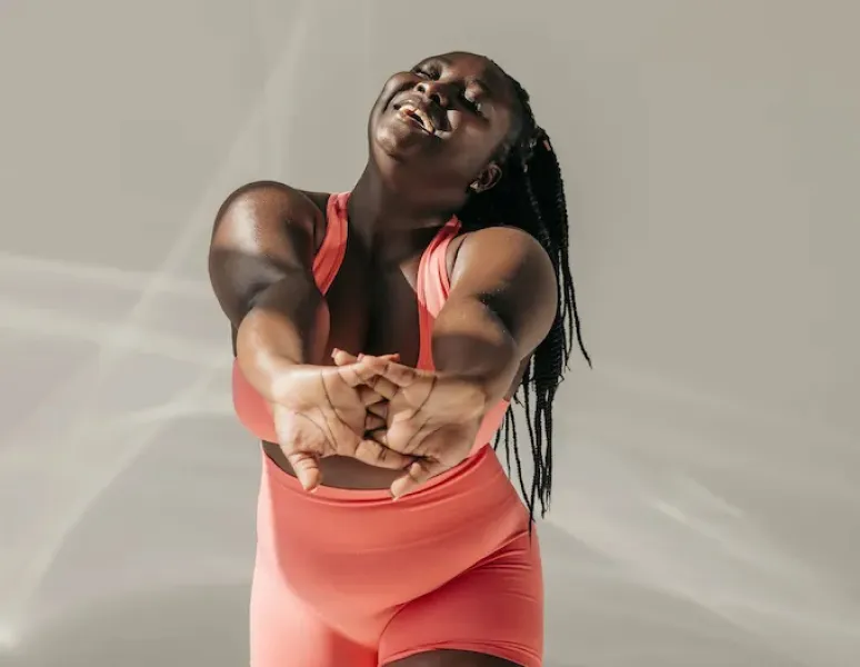 A woman with a round, soft belly smiling and stretching her arms.