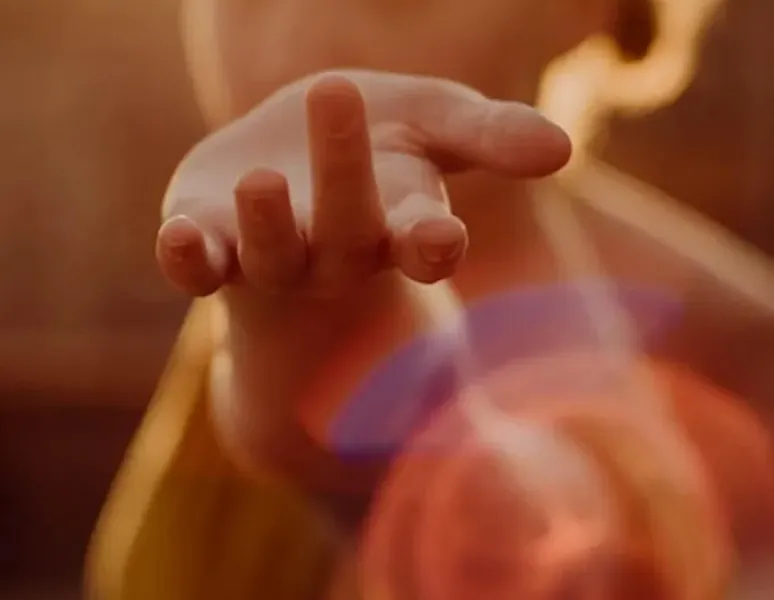 A woman holding up her hand surrounded by light to symbolize the pleasure of pelvic floorgasm.