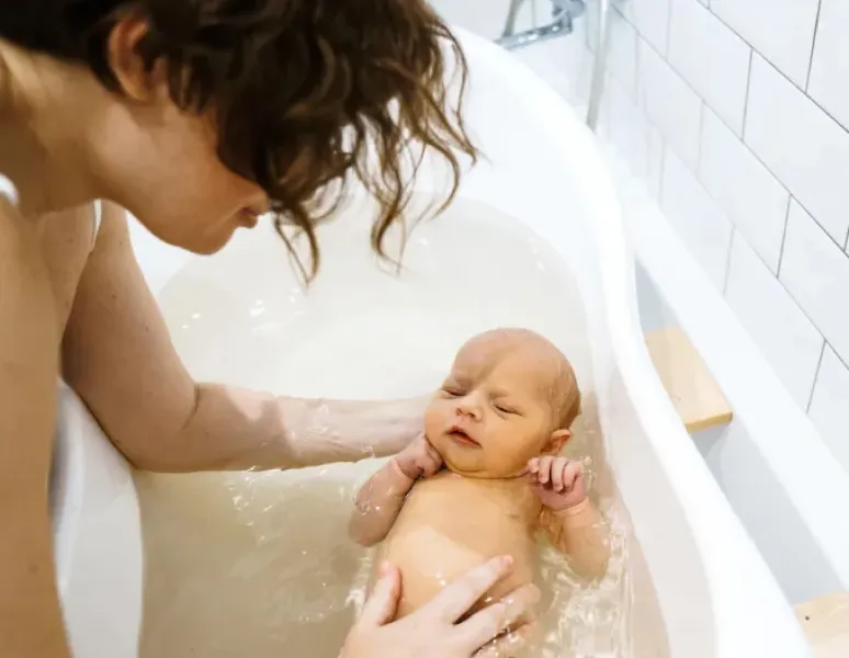 A mom leaning over a bathtub to bathe her baby for a story on physical therapy and proper childcare body mechanics.