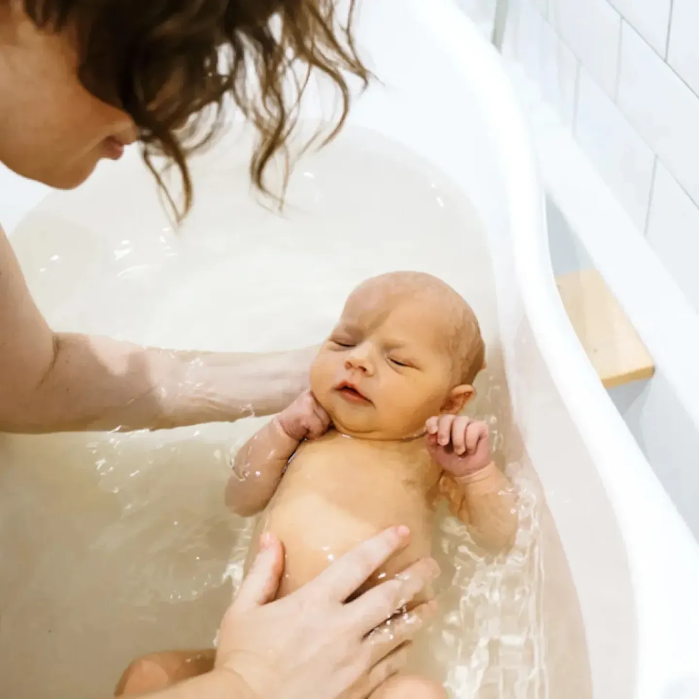 A mom leaning over a bathtub to bathe her baby for a story on physical therapy and proper childcare body mechanics.