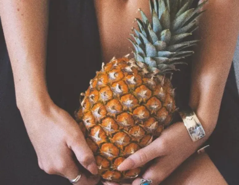 A woman holding a prickly-leaved pineapple in front of her body to symbolize dyspareunia.