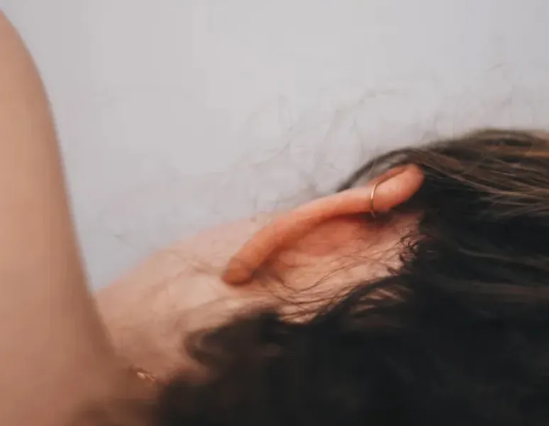 A close-up of a woman's head from the back, she's lying on her side and her hair is pulled back to reveal her ear and neck.