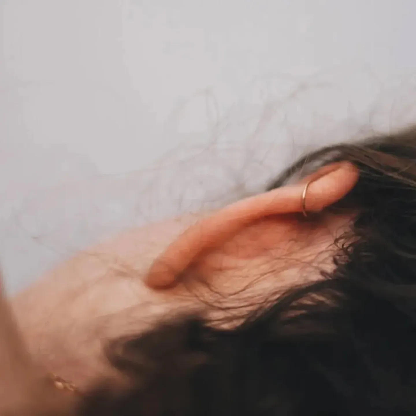 A close-up of a woman's head from the back, she's lying on her side and her hair is pulled back to reveal her ear and neck.