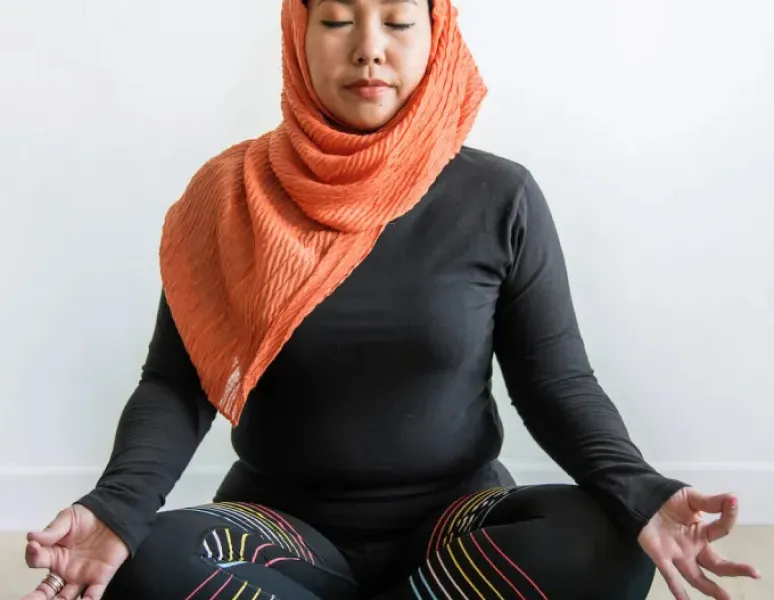 An Islamic woman meditating on a yoga mat.