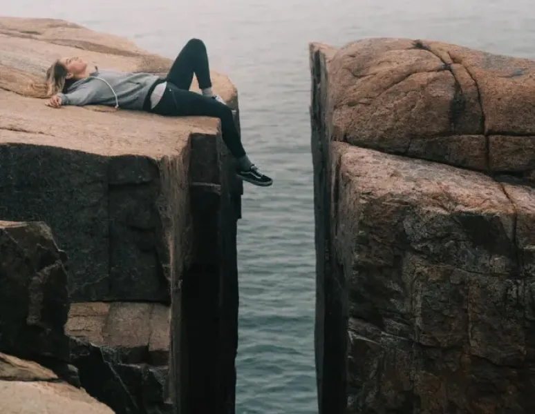 A woman lying next to a huge gap in a rock face.