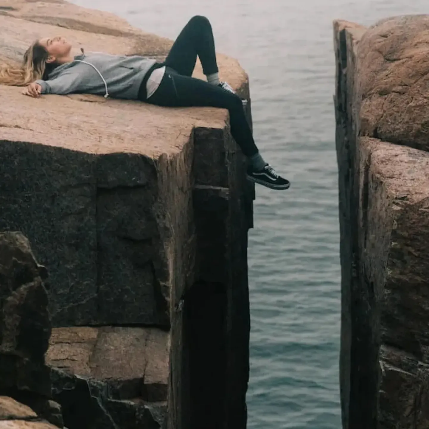 A woman lying next to a huge gap in a rock face.