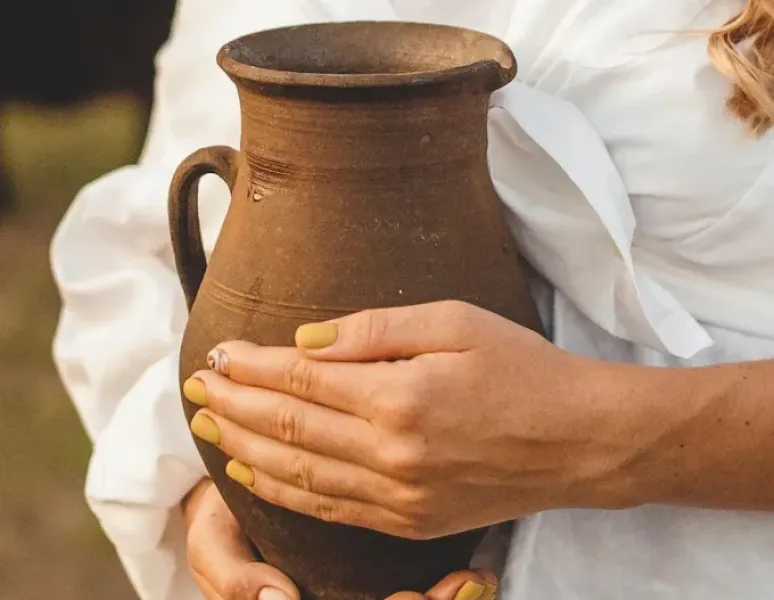 A woman in a white shirt holding an earthenware pitcher in front of her body to represent uterine prolapse.