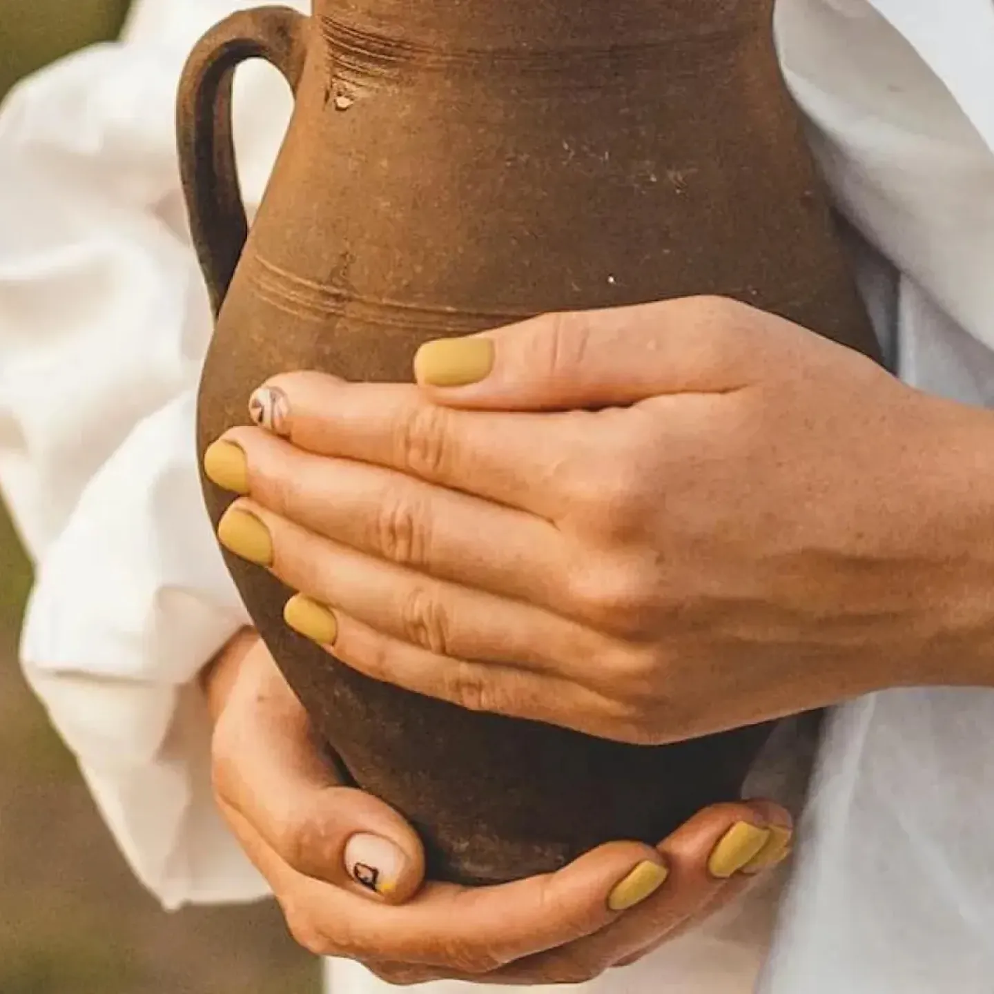 A woman in a white shirt holding an earthenware pitcher in front of her body to represent uterine prolapse.