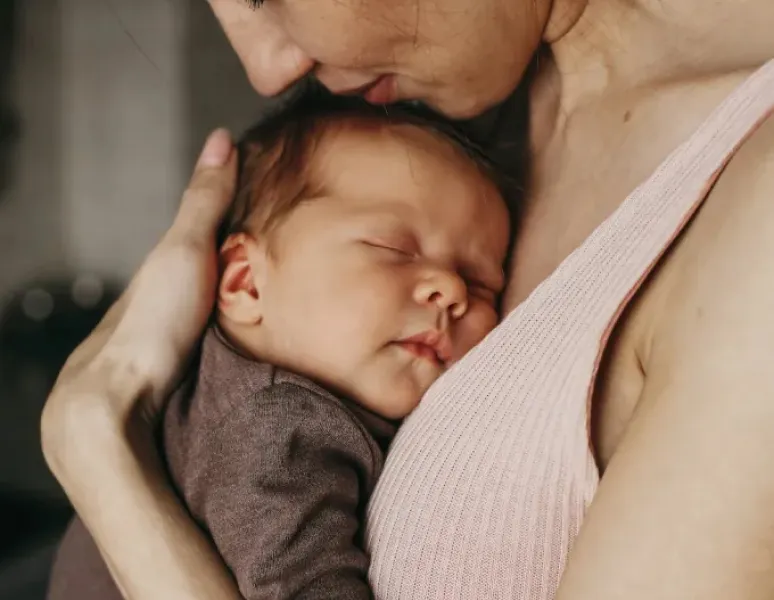 A content mother hugging her sweet, sleeping baby close to her chest.