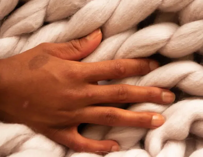 A woman's hand on a blanket with a large, puffy weave.