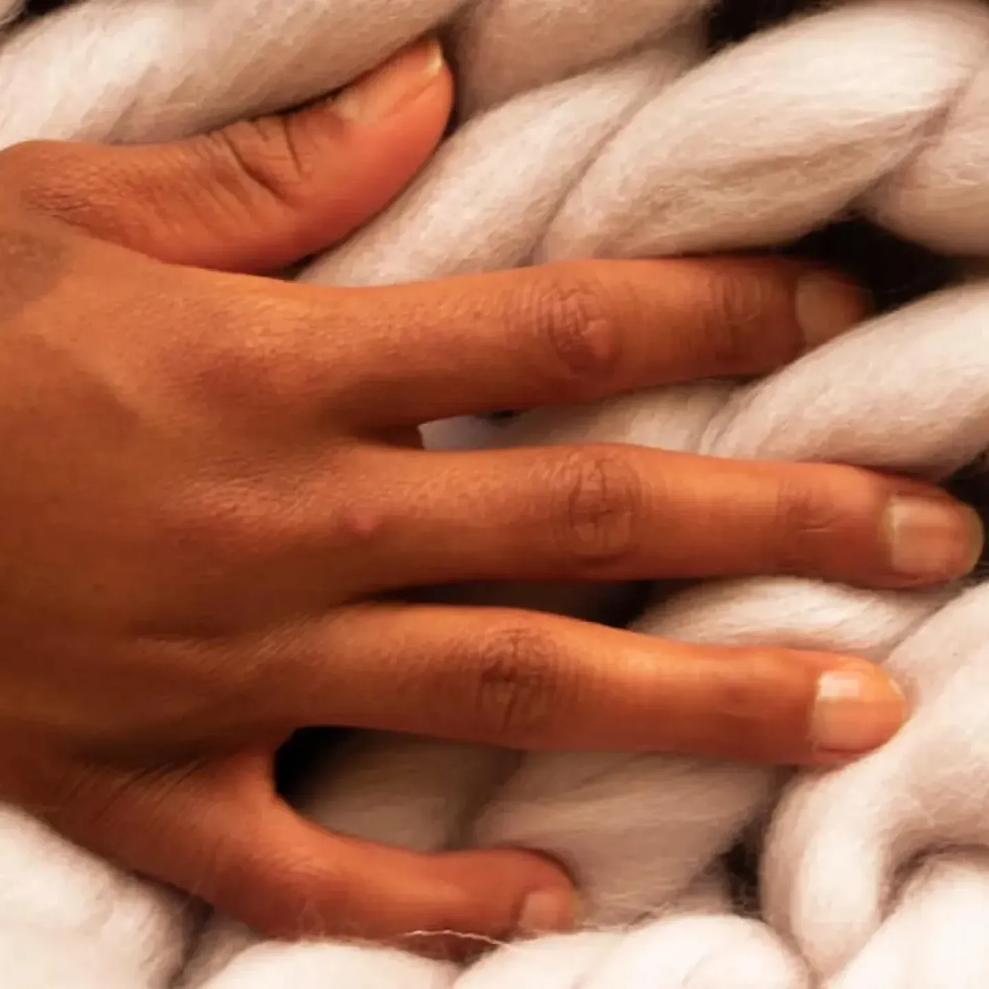 A woman's hand on a blanket with a large, puffy weave.