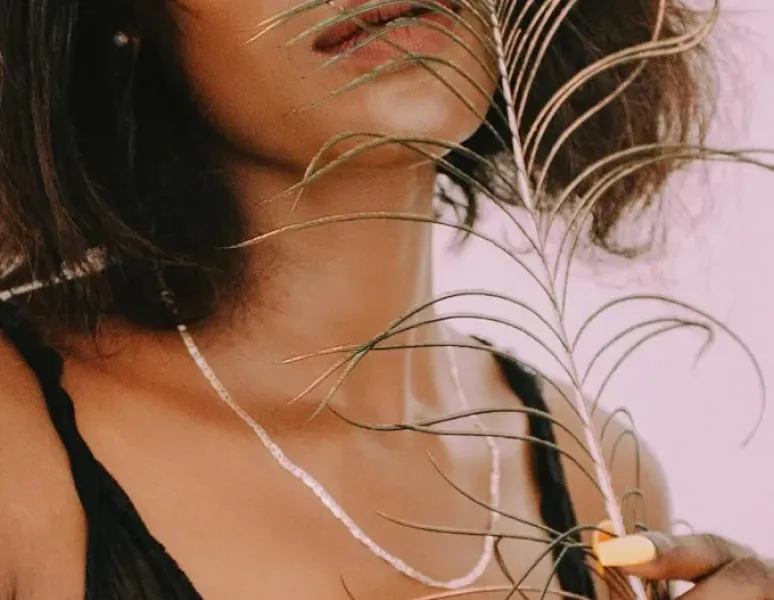 A woman sensually holding a feather up to face.