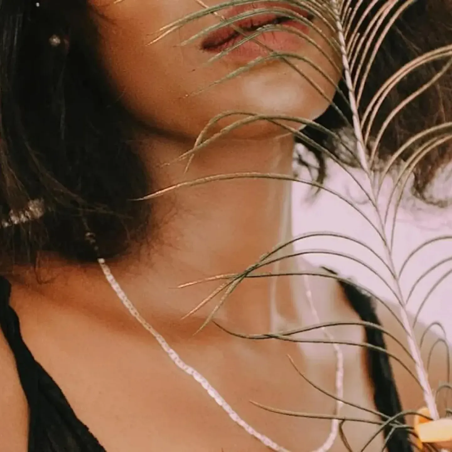 A woman sensually holding a feather up to face.