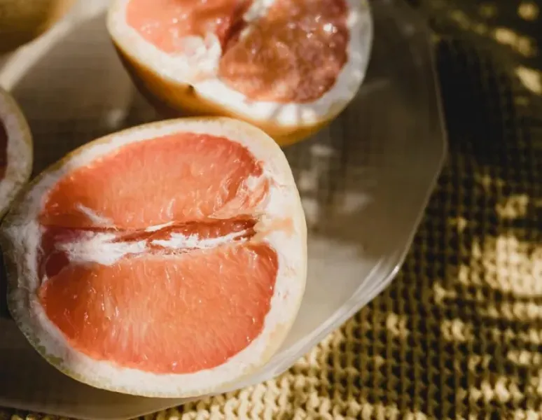 A sliced grapefruit that looks like a vulva on a summer table bathed in dappled sunlight.