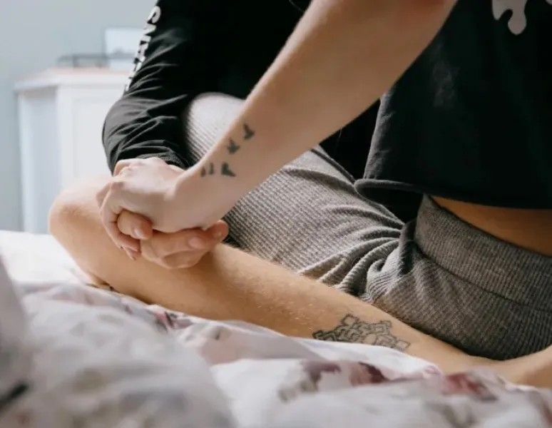 A couple sitting on a bed, holding hands.
