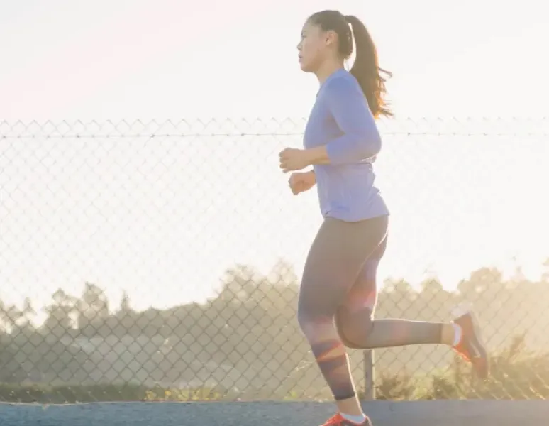 A postpartum woman running at sunset.