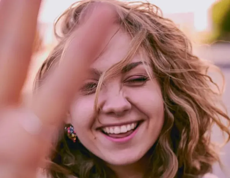 A close-up of an embarrassed woman holding her hand up to partly block her face.
