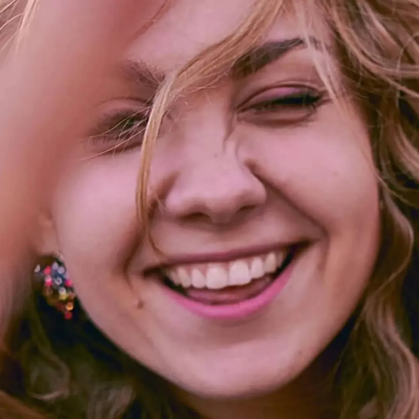 A close-up of an embarrassed woman holding her hand up to partly block her face.